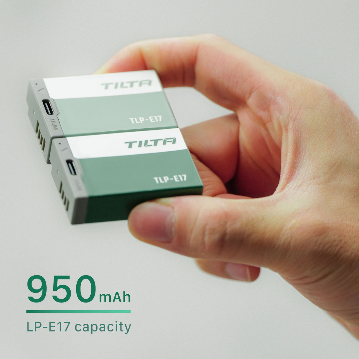 Two Tilta TLP-E17 batteries held between finger and thumb, one Ash Green and one Forest Green, with a 950mAh LP-E17 capacity callout