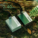 Tilta TNP-W126S batteries in Ash Green and Forest Green charging over USB-C cables on mossy ground, with an approximately 2 hour 40 minute charge time callout