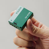 Tilta TNP-W126S battery in Forest Green held in one hand, showing the USB-C input port and the camera contact terminals